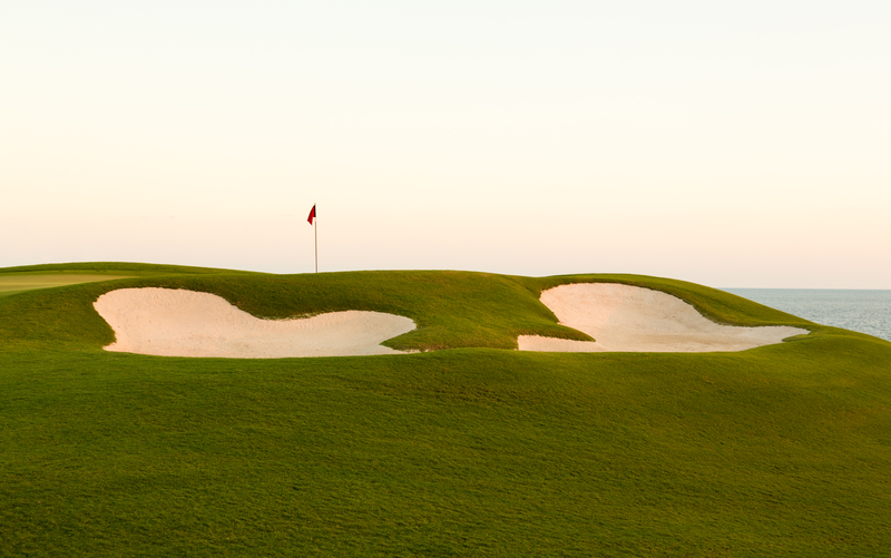 golf hole above sand trap on beautiful oceanfront golf course at sunset